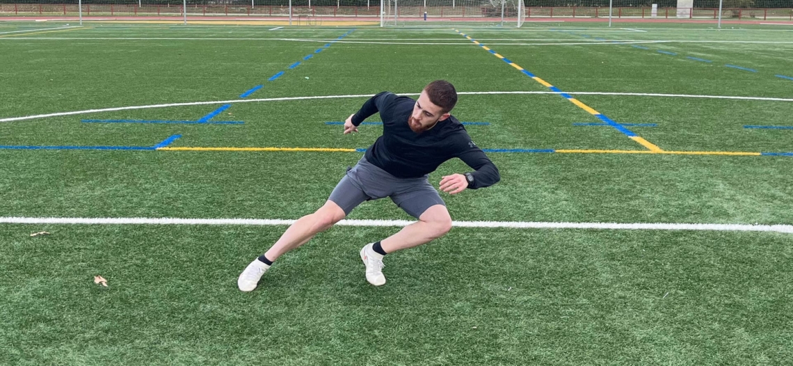 Hombre joven realizando ejercicios en un campo de fútbol.