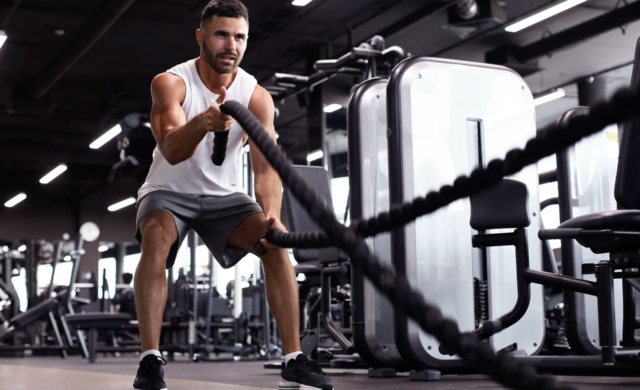 Hombre joven en un gimnasio realizado un ejercicio con cuerdas.