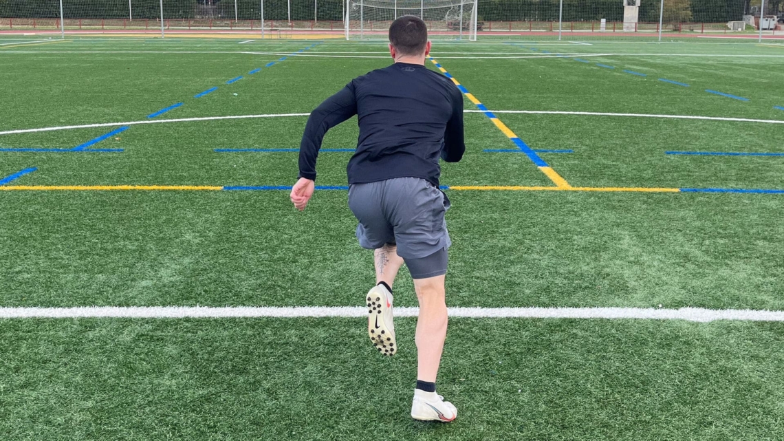 Deportista de espaldas iniciando una carrera en un campo de fútbol.